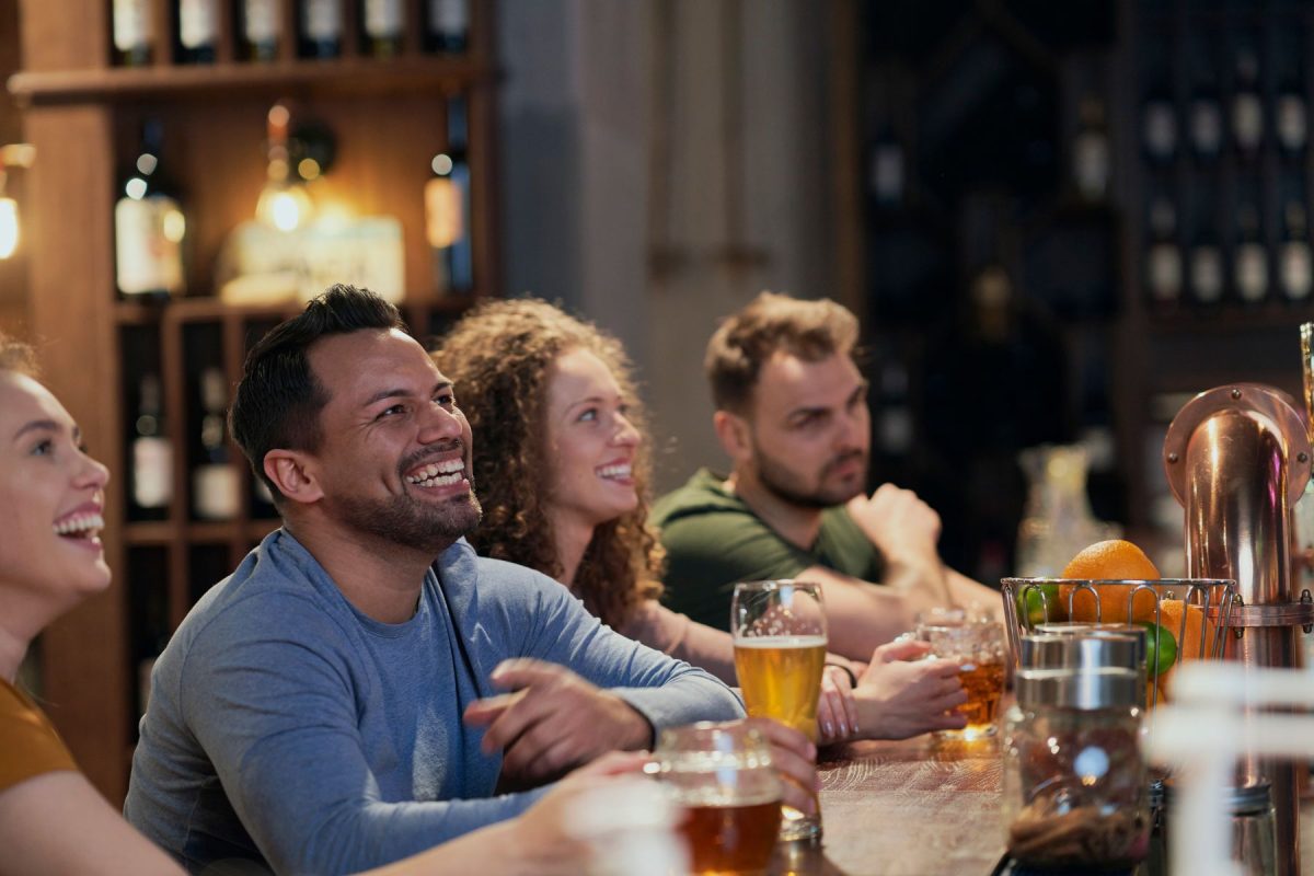 A group of friends laughing and enjoying cold beers at a lively local bar, highlighting the vibrant nightlife and craft brewery scene accessible from Walker Luxury Vacation Rentals in Austin, Texas.